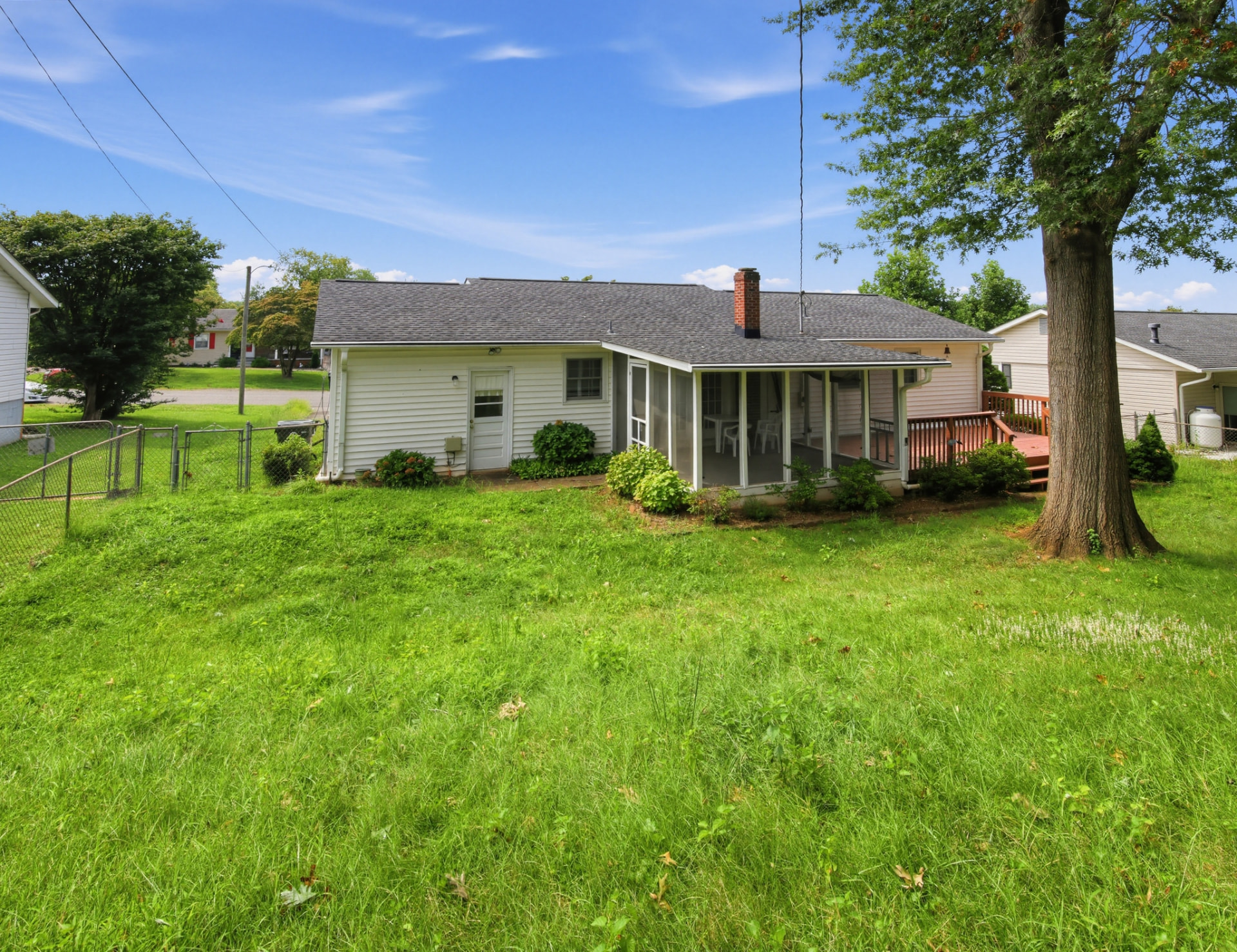 Back of the house with screened porch, wooden deck, fenced yard and a large shade tree